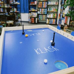 KLASK（クラスク）のゲームボードで磁石を操作し、オレンジ色のボールを打ち合うプレイ風景